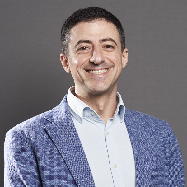 Smiling man in a light blue shirt and blue blazer looking at the camera, professional headshot.